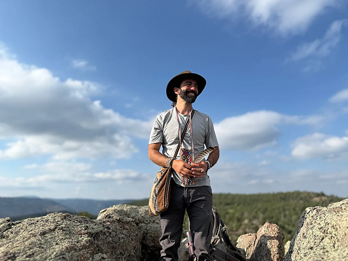 Izzy standing on a rock ledge above the Colorado foothills, a feather in his hands